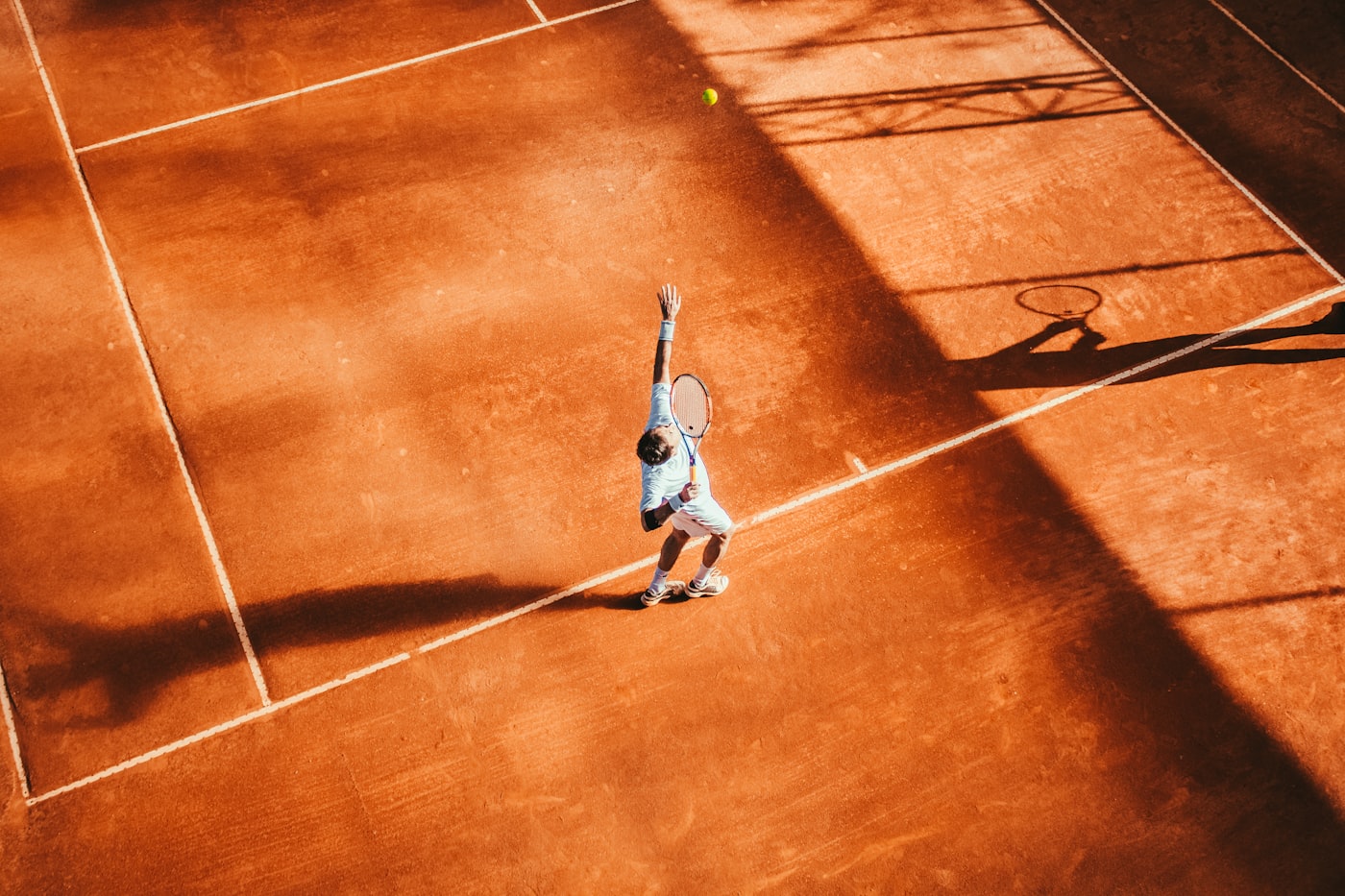 Tennis player serving on a clay court with a yellow tennis ball in the air